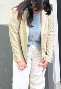 Light beige tailored blazer over a textured light blue shirt and patterned cream trousers. The fabric has a smooth finish and subtle details.