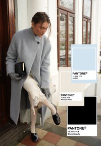 Γυναίκα που φορά μακρύ γκρι παλτό, δαντελένια φούστα, γκρι γάντια και μαύρα παπούτσια, προσαρμόζοντας τα υποδήματά της κοντά σε ξύλινη πόρτα και παράθυρο.