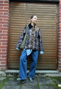 Jachetă cu model în carouri și quilted de culoare maro, cu guler negru, asortată cu o cămașă albastră în carouri, blugi largi de culoare albastră și botine verzi cu toc.