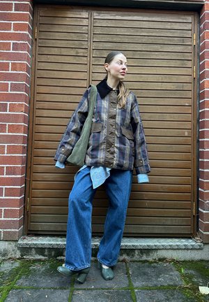Chaqueta acolchada marrón y a cuadros con cuello negro, combinada con una camisa de cuadros azul, vaqueros anchos azules y botines de tacón verde.