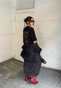 Černé oversized tričko s červeným grafickým potiskem, černá vrstvená bunda, černá kabelka a červené kotníkové boty s špičatými špičkami a podpatky.