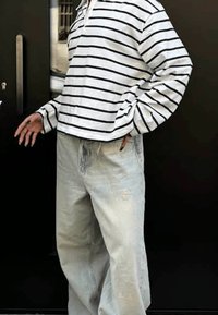 Langärmliges Shirt mit schwarz-weißen Streifen, kombiniert mit hellblauen, weit geschnittenen Jeans, die eine entspannte Passform und sichtbare Stoffstruktur aufweisen.