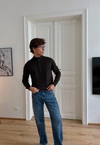 Tamno smeđa košulja dugih rukava s dugmićima, u kombinaciji sa svijetloplavim poderanimfarmerkama ravnog kroja. Glatka tekstura i ležeran kroj.