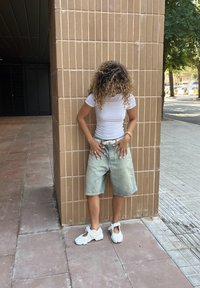 Shorts de ganga de lavagem clara com um ajuste descontraído, t-shirt branca ajustada e sapatilhas brancas. Cabelo encaracolado e acessórios em destaque.