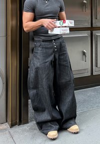 Džínsy s širokými nohavicami, tmavomodré, vysoký pás, s viacerými gombíkmi a hladkou textúrou; v kombinácii s svetlohnedými drevákmi.