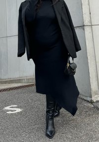 Črna rebrasta obleka z asimetričnim robom, zaprta pod črnima teksturiranim blazerjem. V kombinaciji z črnimi škornji do kolen s peto in majhno torbico.