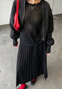 Cazadora bomber negra sobre una blusa de rayas transparente, combinada con una falda negra con pliegues y calcetines rojos. Presenta un bolso rojo y un detalle en capas en las mangas.