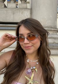 Transparante zonnebril met oranje lenzen, die een sleek ontwerp toont. Verfraaid met een kralenketting met een zeester hanger en schelpen.