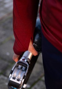 Person iført rød ærme holder en slank, metallisk protetisk ben med et carbon fiber-sokkel og mekanisk knæled.