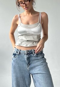 Grijze tanktop met witte accenten, aansluitend ontwerp, gelaagd uiterlijk. Lichtblauwe high-waisted jeans met een relaxed fit en vervaagde textuur.