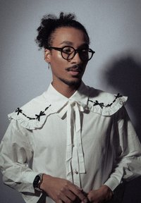 Chemise en coton blanche avec un col à volants, ornée d'accents en ruban noir. Manches longues et fermeture boutonnée à l'avant. Design minimaliste, tissu texturé.