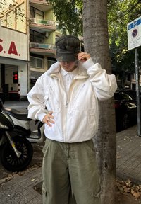 Valge bomber-tagi pehme voodriga, lukuga taskutega, kantud kraega särgi kohal ja sobitatud oliivroheliste cargo-pükstega.