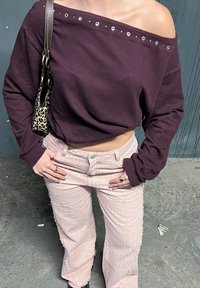 Burgundy off-shoulder topp i bomull med silverfärgade öljett; ljusrosa texturerade högmidjade byxor med fransade fållar. Handväska i leopardsort.