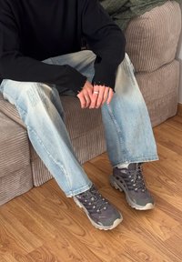 Grå sneakers med texturerad mesh-ovandel och gummisula. Bärs med blå slitna jeans och en svart tröja med fransiga ärmslut.