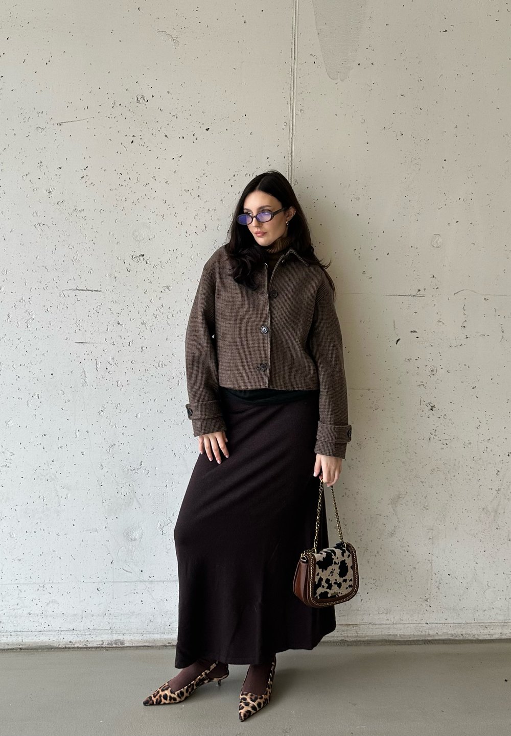 Καφέ, υφασματινή κοντή ζακέτα με λεπτομέρειες από κουμπιά πάνω από μαύρη μπλούζα, συνδυασμένη με μακριά μαύρη φούστα, γόβες λεοπάρ και τσάντα με σχέδιο.