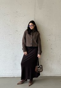 Καφέ, υφασματινή κοντή ζακέτα με λεπτομέρειες από κουμπιά πάνω από μαύρη μπλούζα, συνδυασμένη με μακριά μαύρη φούστα, γόβες λεοπάρ και τσάντα με σχέδιο.