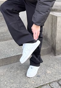 Zapatillas Nike de piel blanca con detalles perforados y un acabado suave, combinadas con pantalones negros de corte ligeramente holgado.