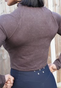 Haut court marron foncé avec un col montant, en tissu lisse, présentant une texture subtile et des coutures ; associé à des leggings noirs taille haute.