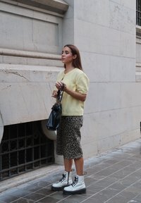 Bijele vojne čizme sa vezicama, žuti pulover kratkih rukava i suknja s leopard uzorkom. Drži malu crnu torbicu.