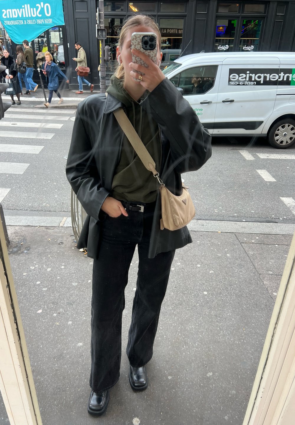 Μαύρα φαρδιά τζιν παντελόνια, πράσινη κουκούλα, μαύρο δερμάτινο μπουφάν και χοντρά μαύρα μποτάκια. Μπεζ τσάντα ώμου με καμπυλωτό σχήμα. Ανακλαστική επιφάνεια.