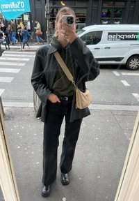 Μαύρα φαρδιά τζιν παντελόνια, πράσινη κουκούλα, μαύρο δερμάτινο μπουφάν και χοντρά μαύρα μποτάκια. Μπεζ τσάντα ώμου με καμπυλωτό σχήμα. Ανακλαστική επιφάνεια.