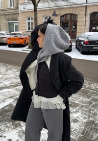 Manteau noir à rayures fines, capuche en laine grise, haut rayé, volants blancs superposés à l'ourlet, pantalon gris, rue enneigée avec voitures garées en arrière-plan.