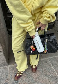 Rumena flis trenirka, črna torba s charms, bela plastenka za vodo označena z "lululemon," in rjavi ter burgundski superge z rumenimi vezalkami.