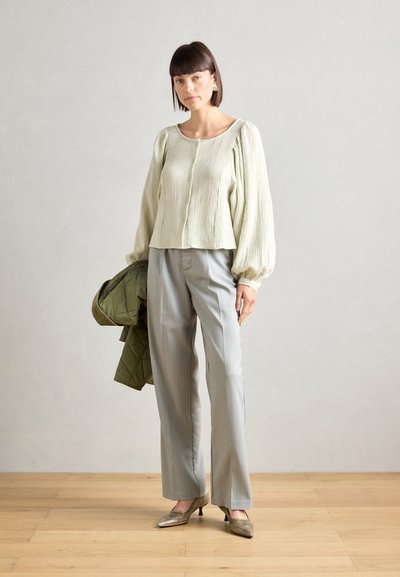 Blusa de textura verde clara con mangas abullonadas, con botones en el frente; combinada con pantalones gris de rayas y tacones metálicos. Chaqueta acolchada verde caída.