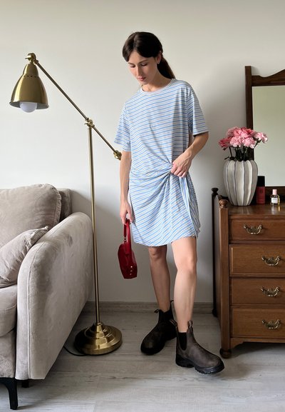 Vestido corto a rayas en azul y blanco con detalle anudado en la cintura, combinado con botas de tobillo marrón oscuro y un bolso rojo.