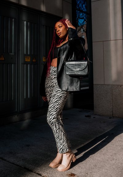 Blazer de cuero negro sobre un top corto negro, pantalones de estampado de cebra y botas tobilleras de color beige claro. Combinado con un bolso metálico plateado.