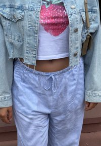 Gaiši zili un balti svītroti brīvi bikses ar elastīgu jostu. Valkā ar īsu baltu T-kreklu, kuram ir rozā zemeņu grafika, un džinsu jaku.