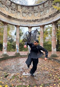 Homme en tenue noire fluide et lunettes de soleil sautant à l'intérieur d'une structure circulaire en pierre avec des colonnes, entourée de feuilles d'automne et de graffitis.
