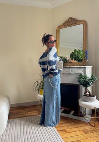 Trikotaža s plavim i sivo prugama, uparena s dugom traper suknjom. Dodatci uključuju srebrnu torbu i okrugle sunčane naočale.