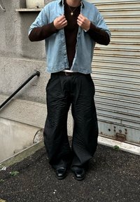 Chemise en jean, pull marron et pantalon large noir. Présente un motif texturé, un design décontracté et des chaussures noires. Collier simple en bronze.