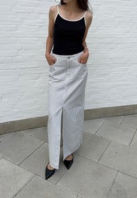 Μαύρο κοντομάνικο μπλουζάκι με λευκές τιράντες, συνδυασμένο με μακριά ριγέ φούστα με μπροστινό σκίσιμο και μαύρες γόβες με μυτερή μύτη.