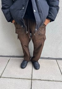 Καφέ cargo παντελόνια με πολλές τσέπες, με σχέδιο κορδόνι στη μέση και λεία υφή, σε συνδυασμό με μαύρα παπούτσια με επένδυση που φοριούντ�αι εύκολα.