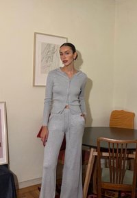 Gai pelēks ribots zip-up hoodie ar atbilstošām flared trenirkotēm. Abiem apģērba gabaliem ir brīva piegriezuma un mīksta auduma tekstūra.