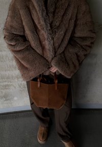 Manteau en fausse fourrure marron avec un profond décolleté en V, sac cabas en daim marron, pantalon marron, et chaussures marron douces, présentant un look superposé et confortable.