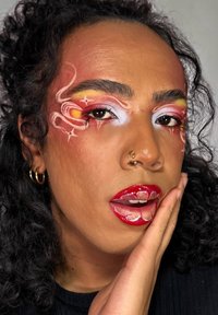 Porträttet har djärv, färgglad makeup med röda, rosa och vita accentfärger. Blanka röda läppar och intrikata mönster runt ögonen ger detaljer.