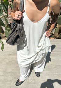 Fehér, laza tank top mély dekoltárral, világos színű, bő nadrággal párosítva. Szürke kézitáska cipzárakkal és textúrázott fekete cipők.