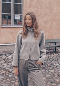 Γκρι φλις μπουφάν με ψηλό γιακά, φερμουάρ και φαρδιά μανίκια, σε συνδυασμό με αντίστοιχες γκρι παντελόνες. Λείο υλικό, μινιμαλιστικός σχεδιασμός.