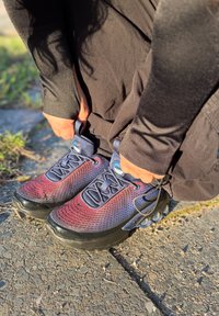 Personne serrant les lacets des baskets rouges et bleues tout en se tenant sur un sol pavé extérieur, en plein soleil.