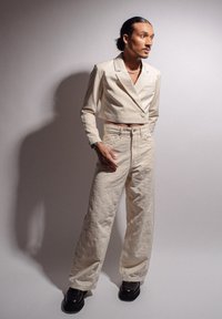 Geknipte beige blazer met een enkele knoop, gecombineerd met gestructureerde beige wijde broek. Draag het met stevige zwarte schoenen en gelaagd sieraden.