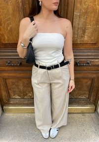 Λευκή τοπ χωρίς τιράντες, μπεζ παντελόνι φαρδύ, μαύρη ζώνη με στρογγυλή αγκράφα, ασημένιο βραχιόλι, μικρή μαύρη τσάντα, λευκά αθλητικά παπούτσια με μαύρες λεπτομέρειες.