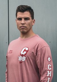 Μακρυμάνικο ροζ πουκάμισο με στρογγυλή λαιμόκοψη, που διαθέτει λευκά και κόκκινα γραφικά: "C" και "66" μπροστά, λογότυπο "CHICAGO" στο μανίκι.