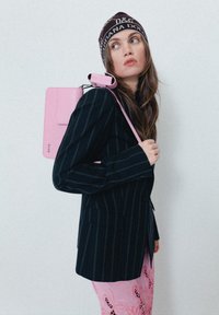 Blazer preto riscado com mangas longas, combinado com uma saia rosa com padrão e uma mala rosa clara usada como mochila. Gorro castanho de marca.