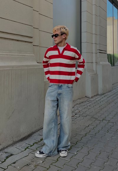 Polo de manga larga a rayas rojas y blancas, jeans de corte relajado en azul claro, zapatillas negras y gafas de sol. Look casual de ropa urbana.