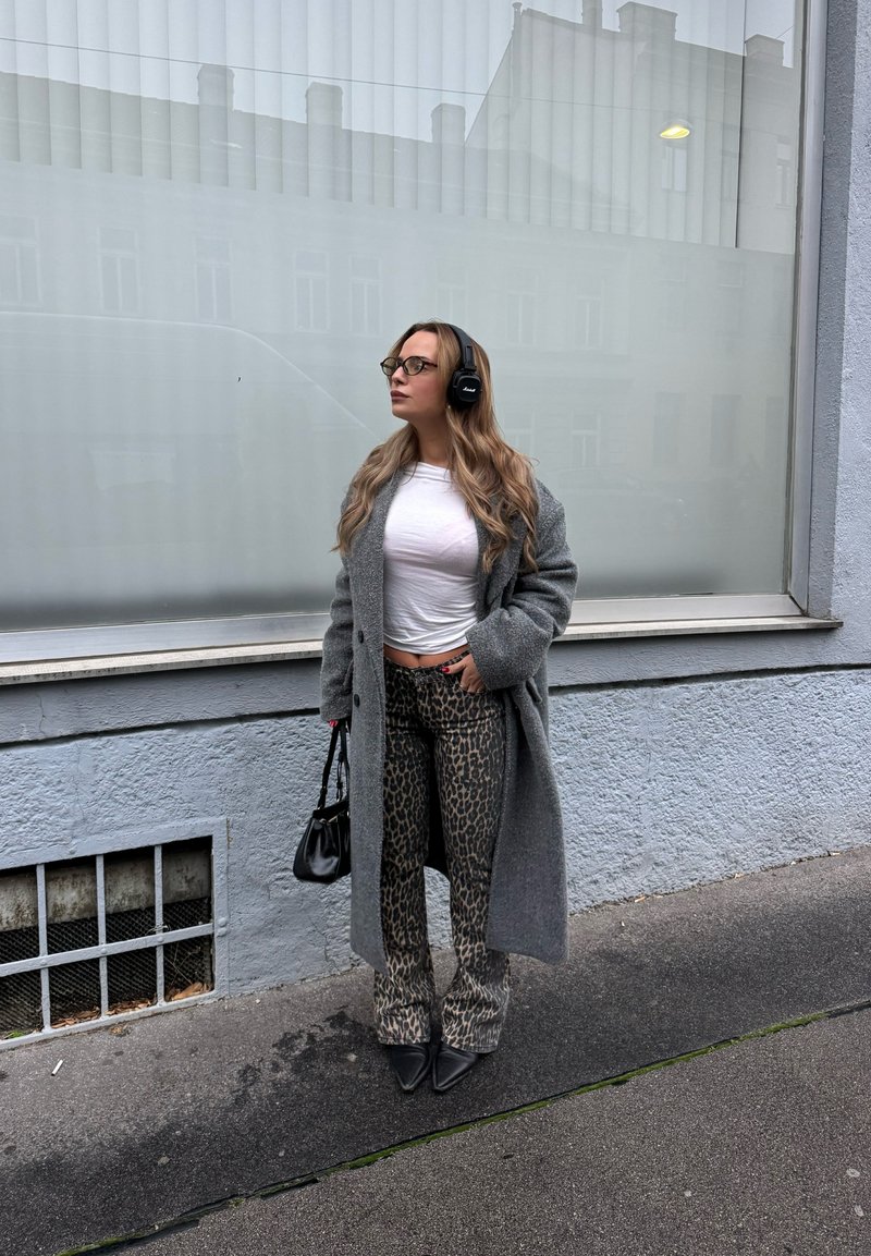 Gray wool coat, white fitted top, leopard print flared pants, and black pointed flats. Accessorized with a small black handbag and headphones.