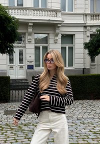 Prugasti pulover s crno-bijelim horizontalnim prugama, upareni s svijetlim širokim hlačama. Tamna torba visi s jednog ramena.