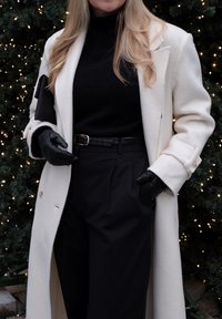 Biely vlnený kabát s veľkými gombíkmi, čierny rolák, čierne nohavice s vysokým pásom, čierne kožené rukavice a textúrované čierne psaníčko.